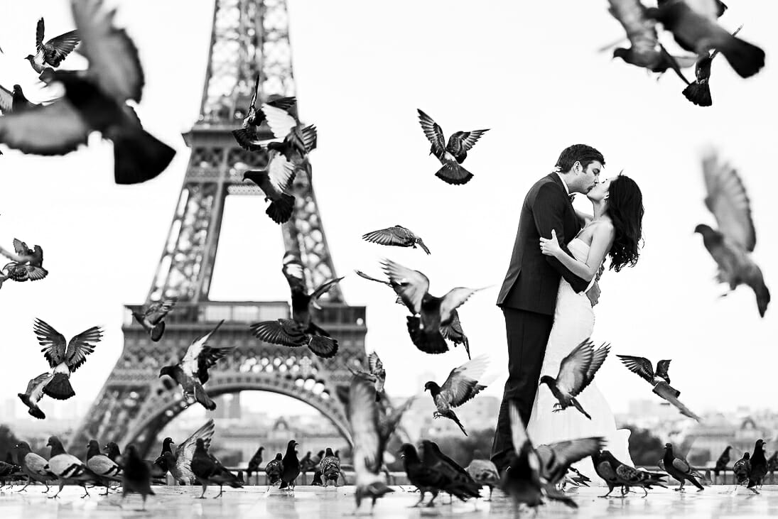 pre wedding photoshoot Eiffel tower in black and white with pigeons flying around the couple