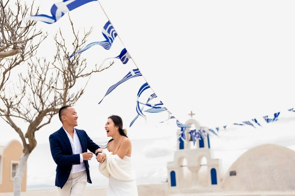 A happily married couple posing together in Santorini with a traditional white church and blue dome in the background, capturing a romantic moment in front of the island's iconic architecture.
