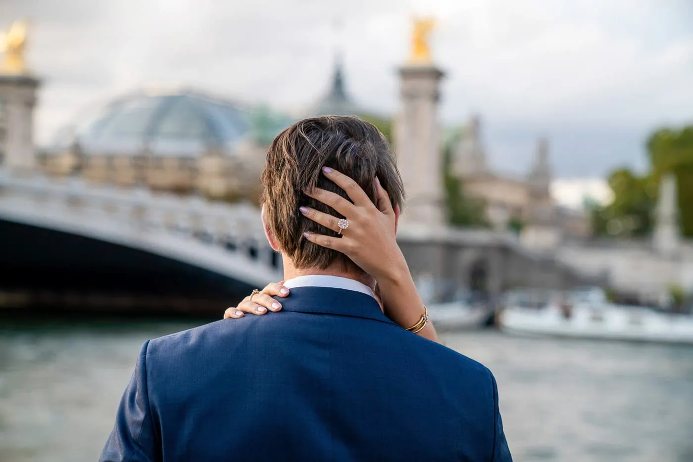 Paris proposal photoshoot with couple showing engagement ring against Alexander III Bridge and Seine River backdrop