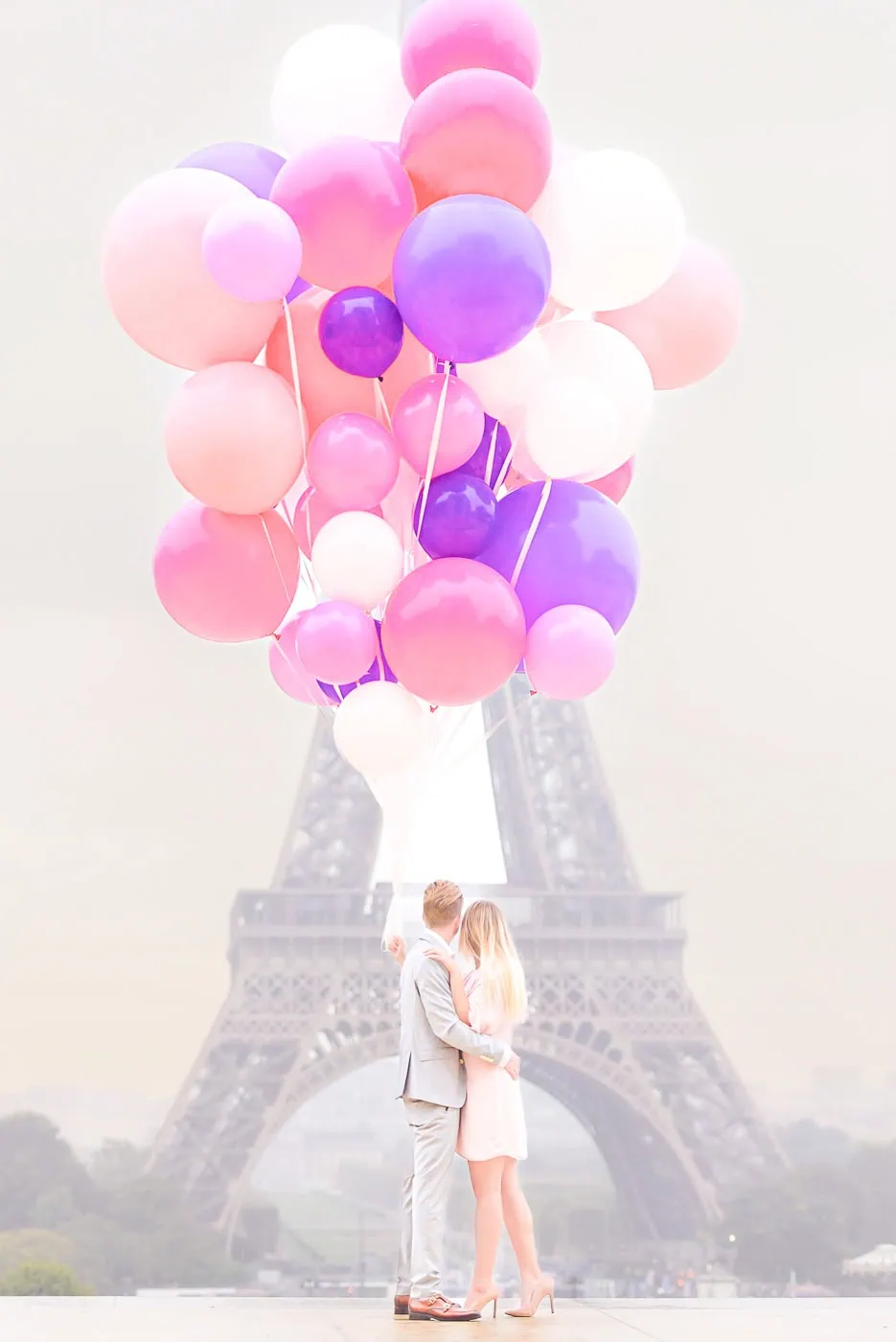 Couple embracing at Trocadéro plaza during sunrise with massive pastel balloon installation and Eiffel Tower backdrop, Paris engagement photography