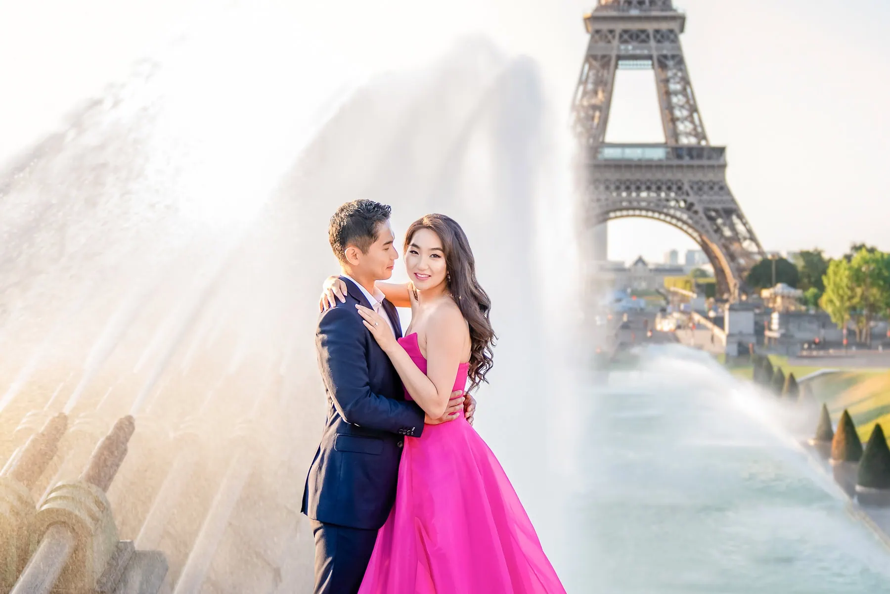 Stunning sunrise Paris photoshoot at Trocadero fountains with couple in pink gown and suit, water spray and Eiffel Tower backdrop