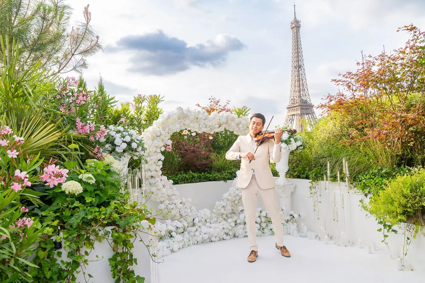 Master violinist in white performing amid silk-floral installations on the private Secret Garden Paris rooftop terrace, with an unobstructed view of the Eiffel Tower—perfect for an intimate proposal.