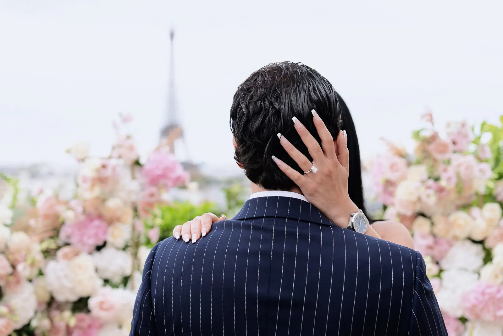 Молодая женщина демонстрирует бриллиантовое обручальное кольцо во время фотосессии на крыше ресторана Peninsula Paris Secret Table на фоне Эйфелевой башни.