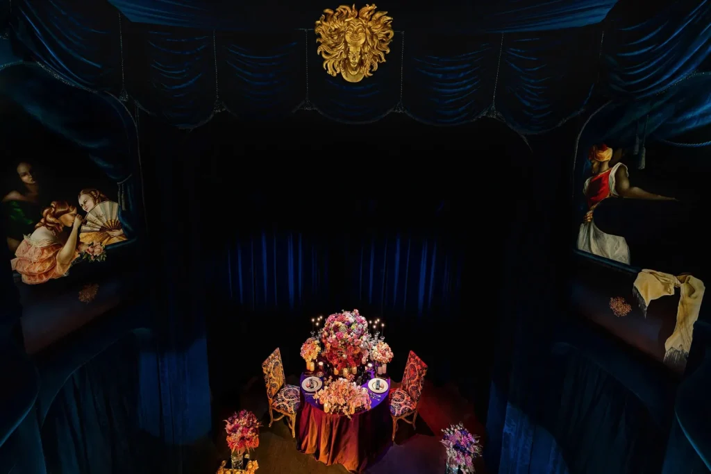 Elegant private theater anniversary dinner setup in Paris featuring lavish floral arrangements, personalized Ladurée macarons, and royal blue theater curtains.