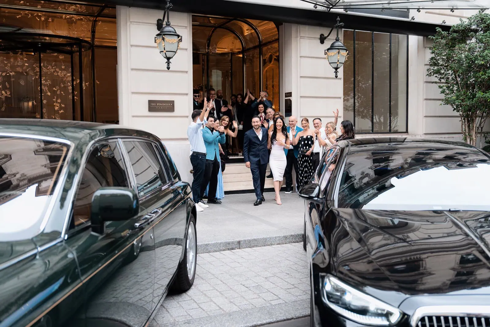 Молодожёны выходят из вестибюля отеля Peninsula Paris под аплодисменты семьи и друзей на фоне зелёного Rolls-Royce и чёрного Mercedes-Maybach.