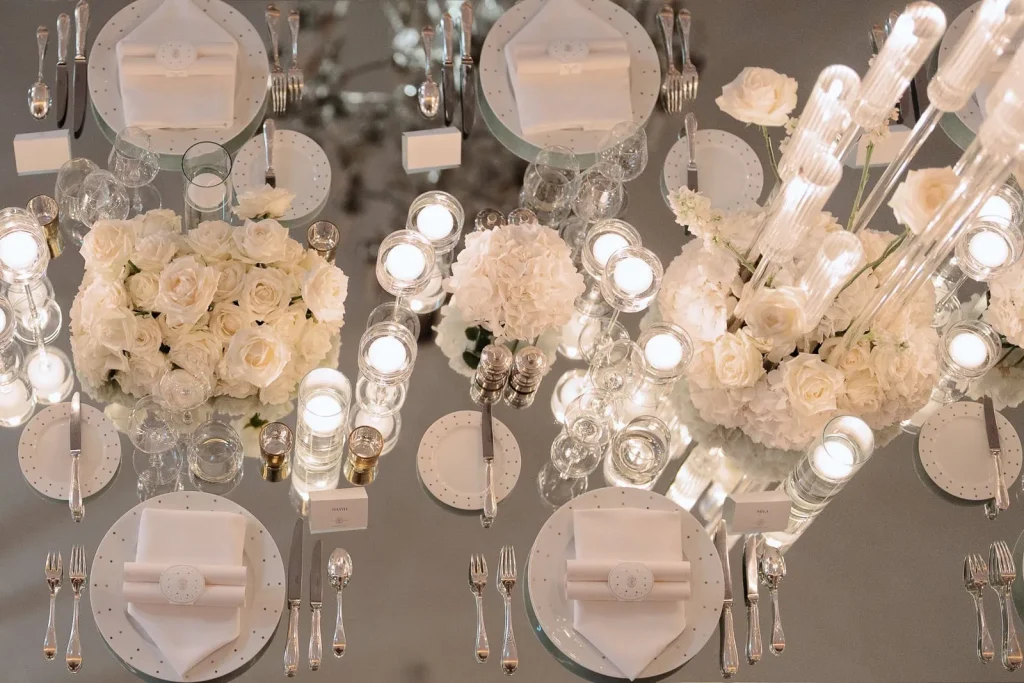 Close-up aerial view of elegant wedding decor featuring all-white roses, candles, and mirrored glass tabletops at Hotel Plaza Athénée, Paris.