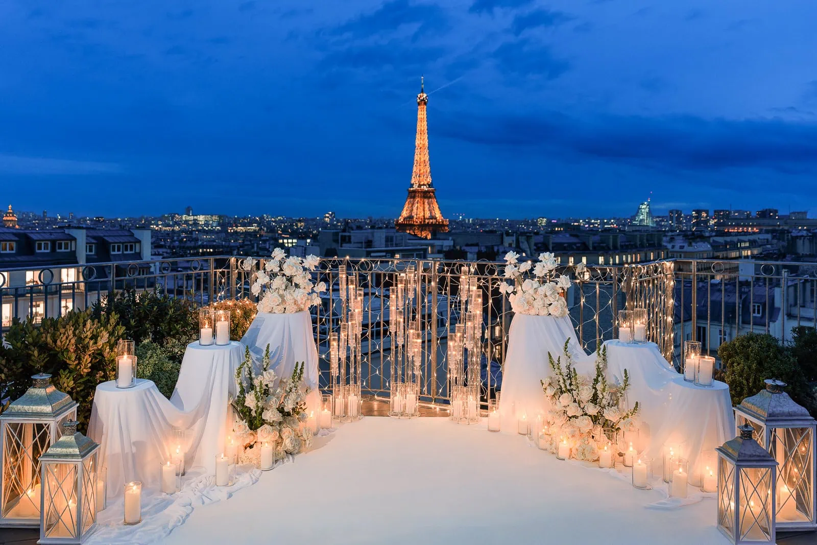 Propuesta de matrimonio privada en la azotea del hotel Copernic en París, al atardecer: arreglos de rosas blancas, manteles de lino blanco, candelabros, luces de hadas como telón de fondo y la Torre Eiffel iluminada.